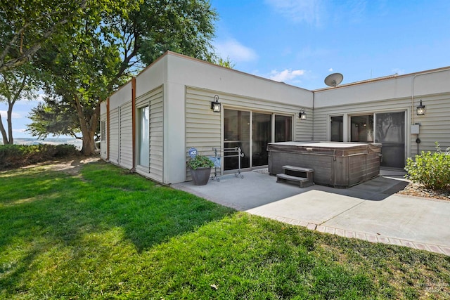 rear view of property featuring a lawn, a patio, and a hot tub