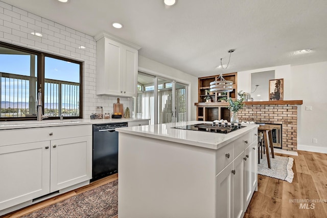 kitchen featuring a kitchen island, a sink, black appliances, light wood-style floors, and white cabinetry