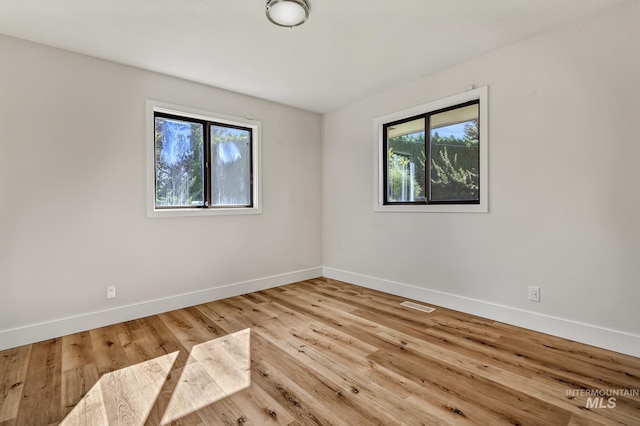 empty room featuring wood finished floors, baseboards, and visible vents