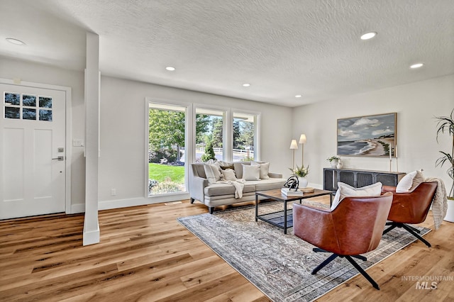 living area featuring light wood finished floors, recessed lighting, a textured ceiling, and baseboards