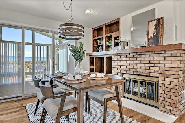 dining room with an inviting chandelier, a textured ceiling, a brick fireplace, and light wood finished floors