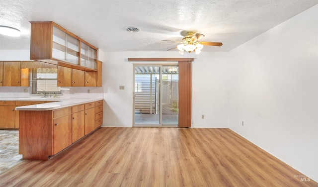 kitchen featuring light wood finished floors, ceiling fan, brown cabinetry, a peninsula, and light countertops