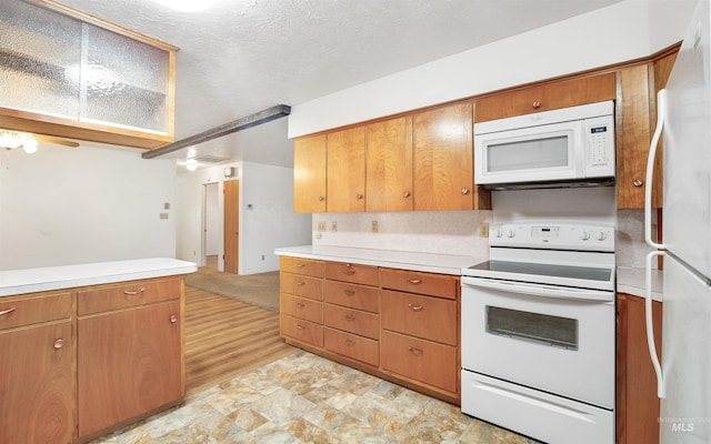 kitchen with a textured ceiling, stone finish floor, brown cabinets, light countertops, and white appliances