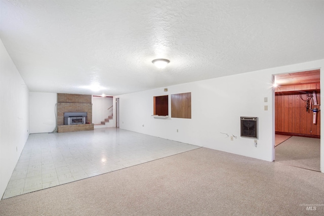 unfurnished living room featuring a brick fireplace, heating unit, stairway, and a textured ceiling