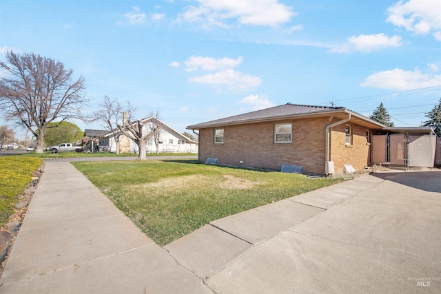 view of property exterior with a yard, aphalt driveway, brick siding, and metal roof