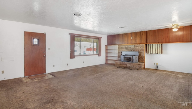 unfurnished living room featuring a fireplace with raised hearth, a ceiling fan, visible vents, carpet, and a textured ceiling