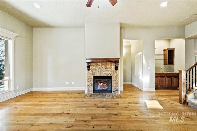 unfurnished living room featuring ceiling fan, light hardwood / wood-style floors, and a tiled fireplace