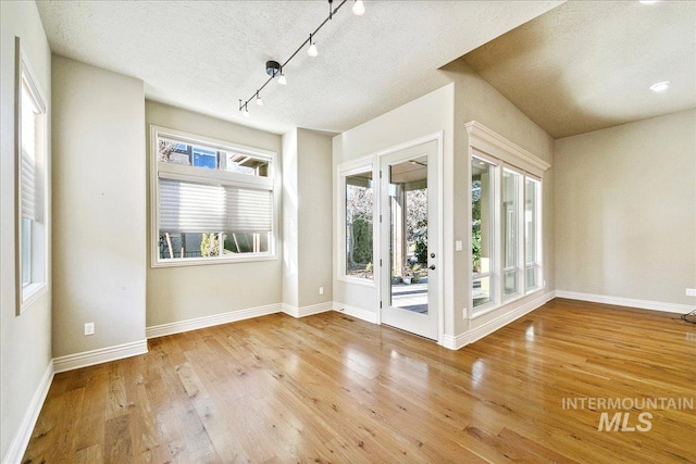 empty room featuring a textured ceiling, light wood-type flooring, and rail lighting