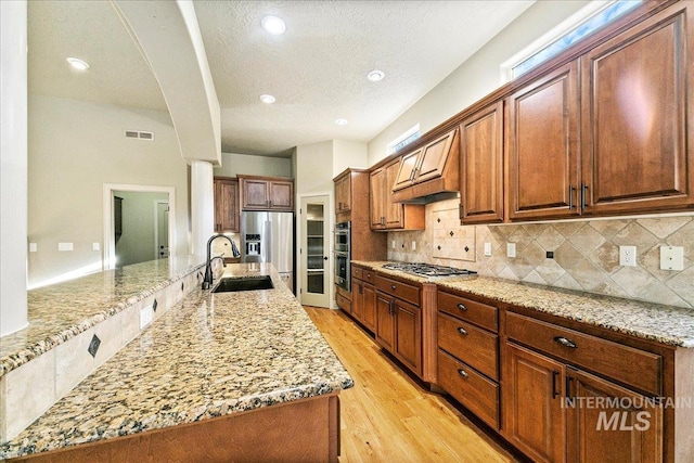 kitchen featuring light stone countertops, backsplash, premium range hood, sink, and light hardwood / wood-style floors