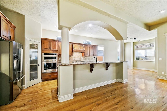 kitchen with backsplash, a kitchen breakfast bar, rail lighting, light stone countertops, and appliances with stainless steel finishes