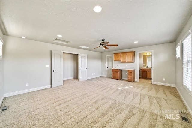 unfurnished living room with light carpet, a textured ceiling, ceiling fan, and sink