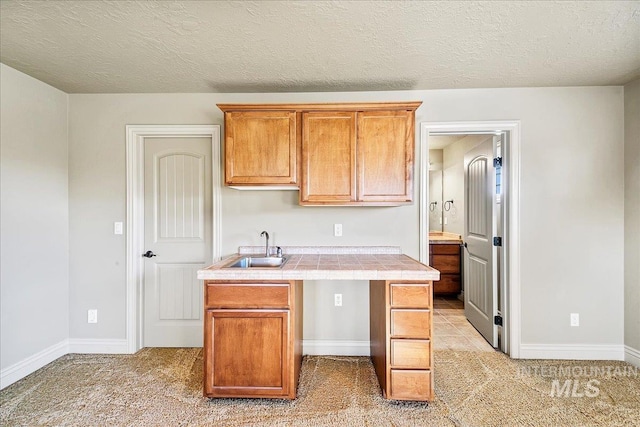 kitchen featuring a textured ceiling, light colored carpet, tile counters, and sink