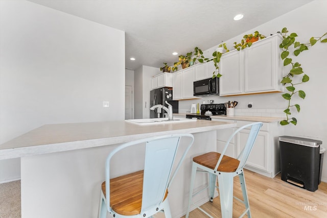 kitchen with black appliances, light wood-type flooring, an island with sink, a kitchen breakfast bar, and white cabinets