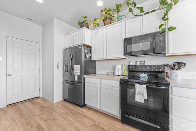 kitchen with white cabinetry, light hardwood / wood-style floors, black appliances, and a textured ceiling