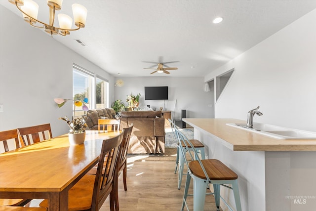 dining space featuring sink, light hardwood / wood-style flooring, and ceiling fan with notable chandelier