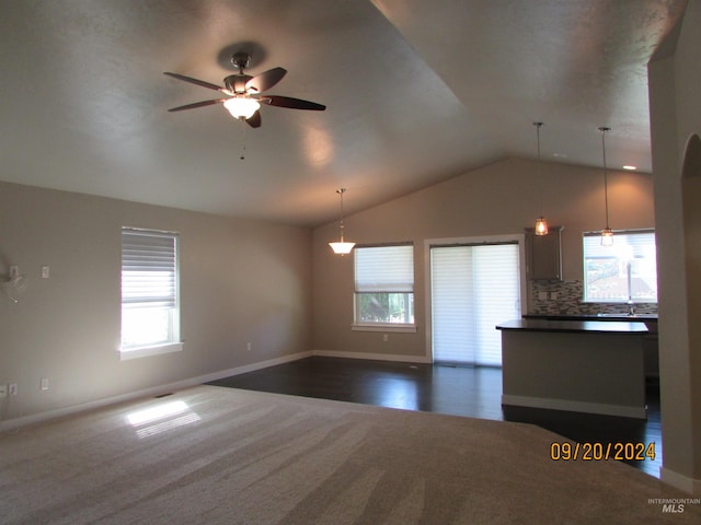 unfurnished living room featuring ceiling fan, lofted ceiling, plenty of natural light, and dark carpet