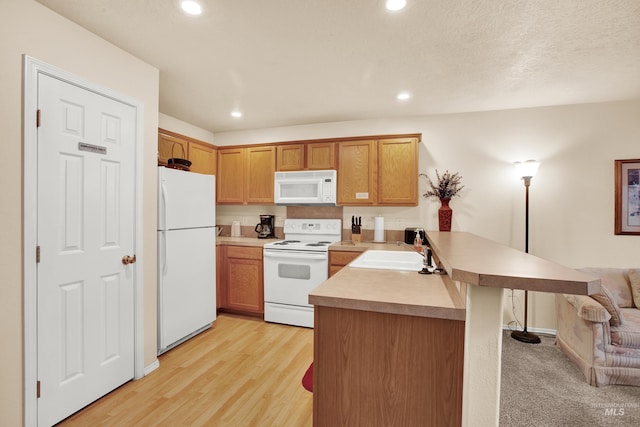 kitchen with a sink, a kitchen breakfast bar, a peninsula, white appliances, and recessed lighting
