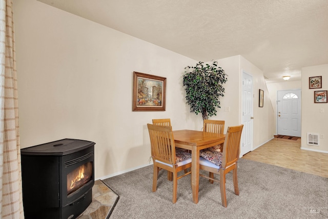 carpeted dining area featuring baseboards, a textured ceiling, visible vents, and a wood stove