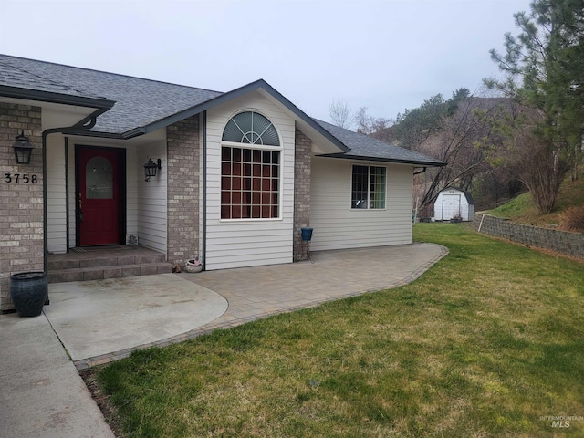 view of exterior entry with brick siding, a patio area, a shingled roof, and a yard