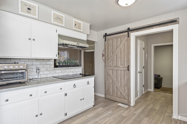 827 Alturas Dr N, Twin Falls, ID 83301 - kitchen with a barn door, custom exhaust hood, tasteful backsplash, black electric cooktop, and white cabinetry
