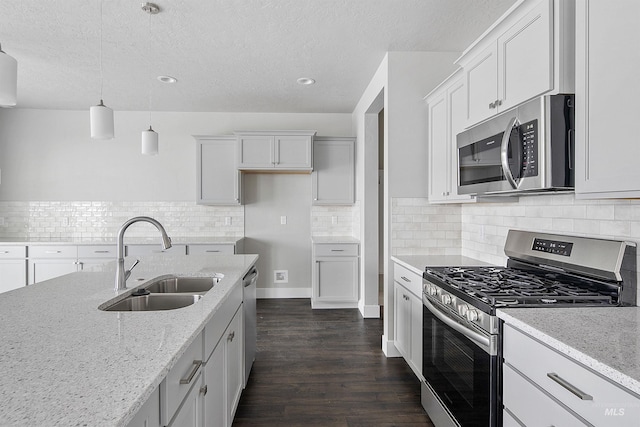 kitchen with dark wood finished floors, hanging light fixtures, appliances with stainless steel finishes, a sink, and light stone countertops