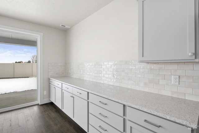 kitchen with light stone counters, visible vents, baseboards, dark wood-style floors, and tasteful backsplash