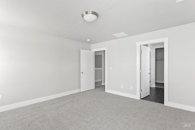 unfurnished bedroom featuring a textured ceiling, carpet flooring, visible vents, baseboards, and a walk in closet