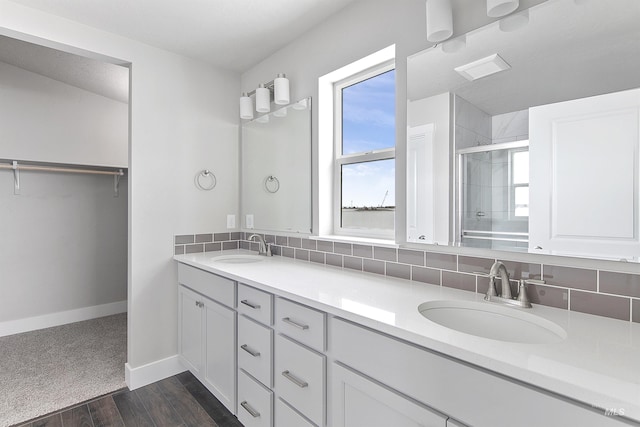 full bath with tasteful backsplash, a stall shower, a sink, and a spacious closet