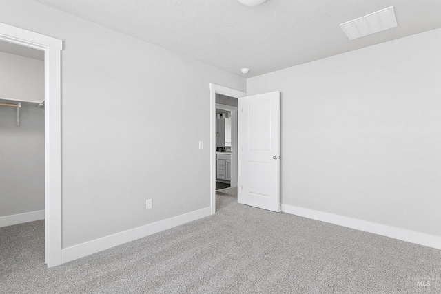 unfurnished bedroom with carpet floors, a walk in closet, visible vents, and baseboards