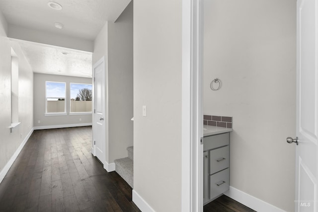 hall featuring dark wood-style flooring, a textured ceiling, baseboards, and stairs