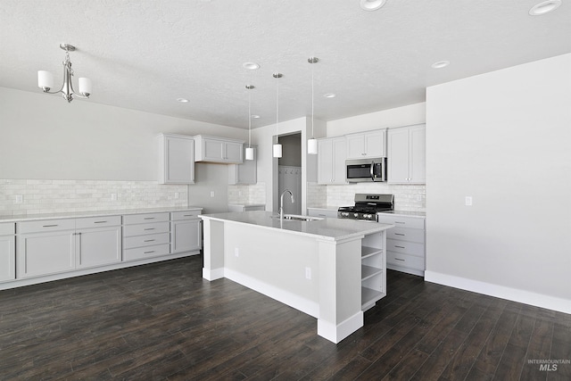 kitchen with dark wood finished floors, open shelves, stainless steel appliances, a kitchen island with sink, and a sink