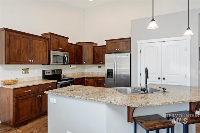 kitchen featuring a breakfast bar area, wood finished floors, a high ceiling, a sink, and stainless steel appliances