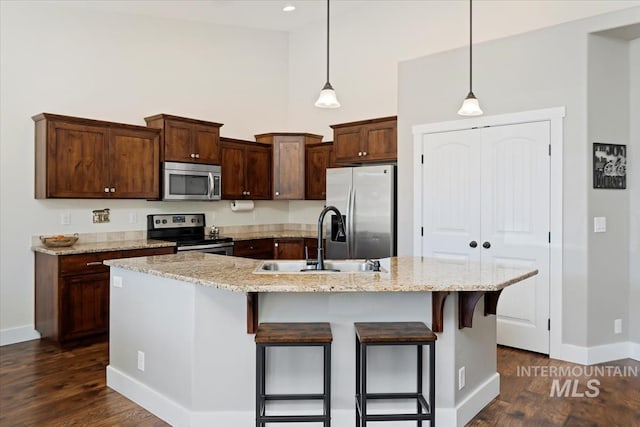 kitchen with baseboards, a breakfast bar, a sink, a towering ceiling, and appliances with stainless steel finishes