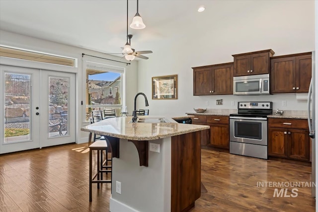 kitchen with a kitchen bar, a kitchen island with sink, a sink, dark wood-style floors, and appliances with stainless steel finishes