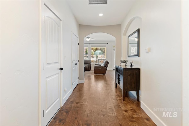 corridor with visible vents, recessed lighting, arched walkways, baseboards, and dark wood-style flooring