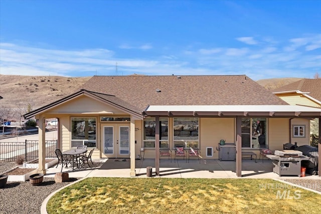 back of property featuring fence, roof with shingles, a lawn, french doors, and a patio area