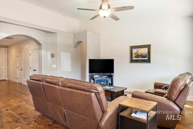 living area featuring ceiling fan, wood finished floors, arched walkways, and baseboards