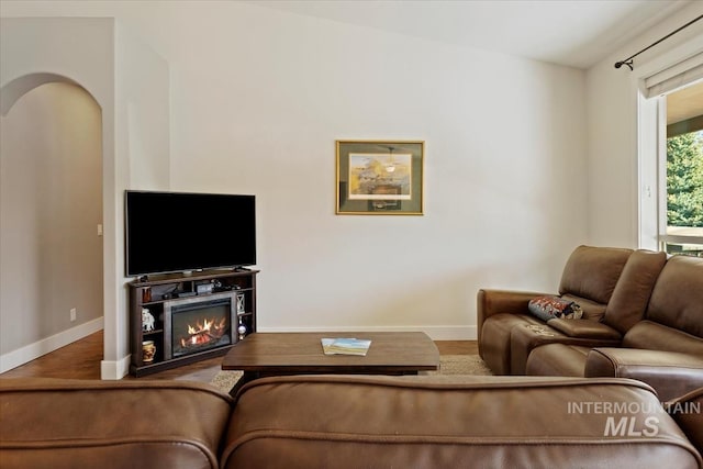 living room featuring arched walkways, baseboards, and wood finished floors