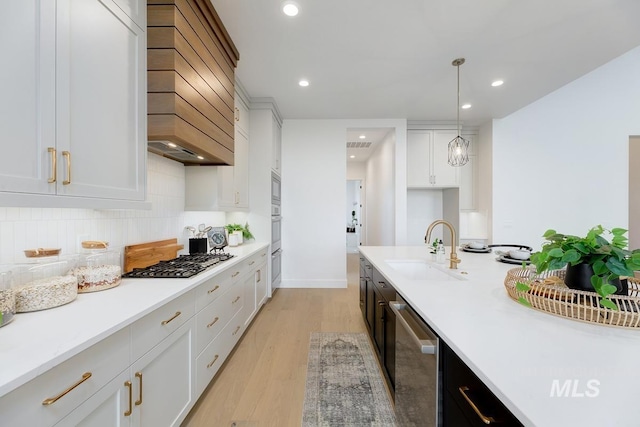 kitchen with sink, light hardwood / wood-style flooring, appliances with stainless steel finishes, decorative light fixtures, and white cabinetry