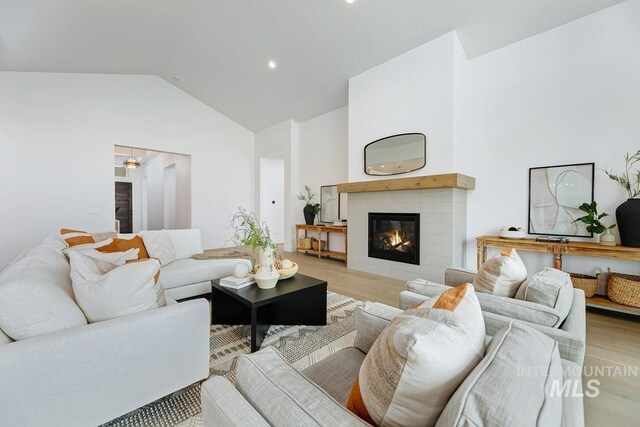 living room with a tile fireplace, light wood-type flooring, and high vaulted ceiling