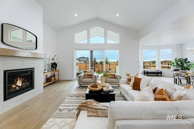 living room with high vaulted ceiling, light hardwood / wood-style floors, an inviting chandelier, and a tiled fireplace