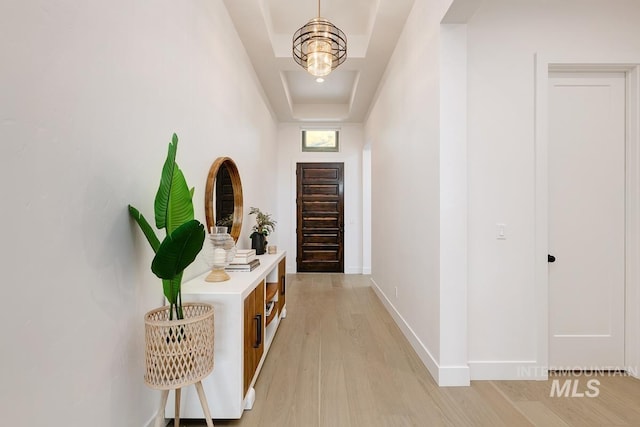 hallway featuring light wood-type flooring, a tray ceiling, and a notable chandelier