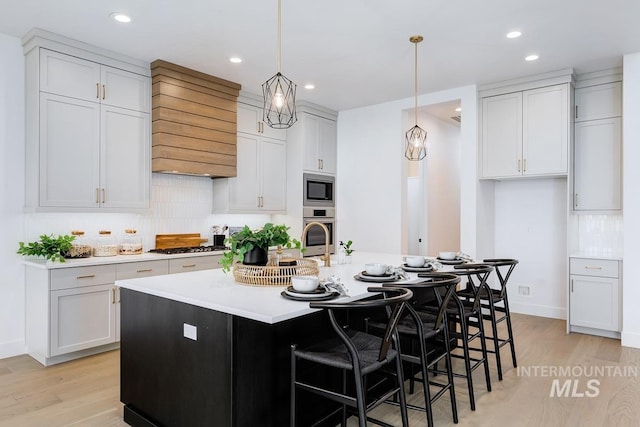 kitchen with white cabinetry, an island with sink, light hardwood / wood-style floors, decorative light fixtures, and appliances with stainless steel finishes