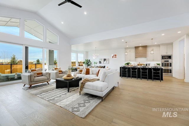 living room with ceiling fan with notable chandelier, high vaulted ceiling, and light hardwood / wood-style flooring