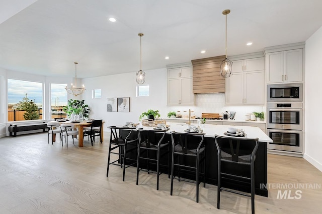 kitchen featuring appliances with stainless steel finishes, light wood-type flooring, a kitchen island with sink, white cabinetry, and a breakfast bar area