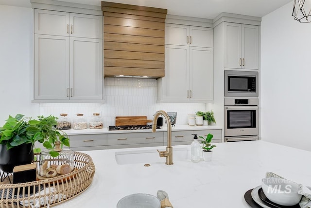 kitchen featuring appliances with stainless steel finishes, backsplash, custom exhaust hood, sink, and hanging light fixtures