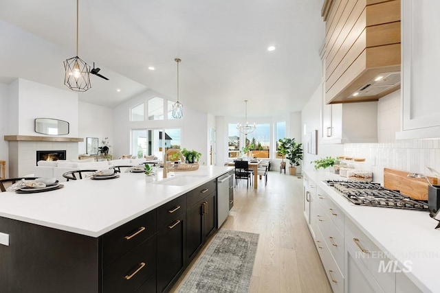 kitchen with white cabinets, custom range hood, a kitchen island with sink, and sink