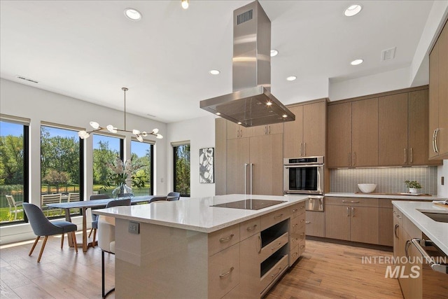 kitchen with island range hood, appliances with stainless steel finishes, a warming drawer, light wood-type flooring, and recessed lighting
