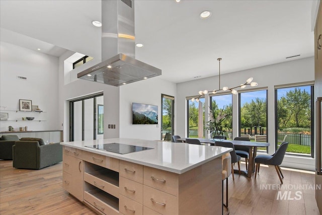 kitchen featuring modern cabinets, island range hood, light brown cabinetry, light stone counters, and open floor plan