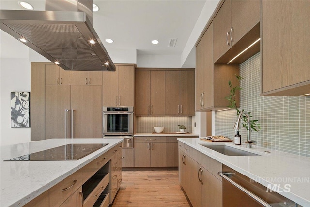 kitchen with stainless steel appliances, a sink, extractor fan, light wood finished floors, and a warming drawer